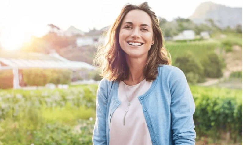 Adult woman standing in a field on a farm looking at the camera, smiling