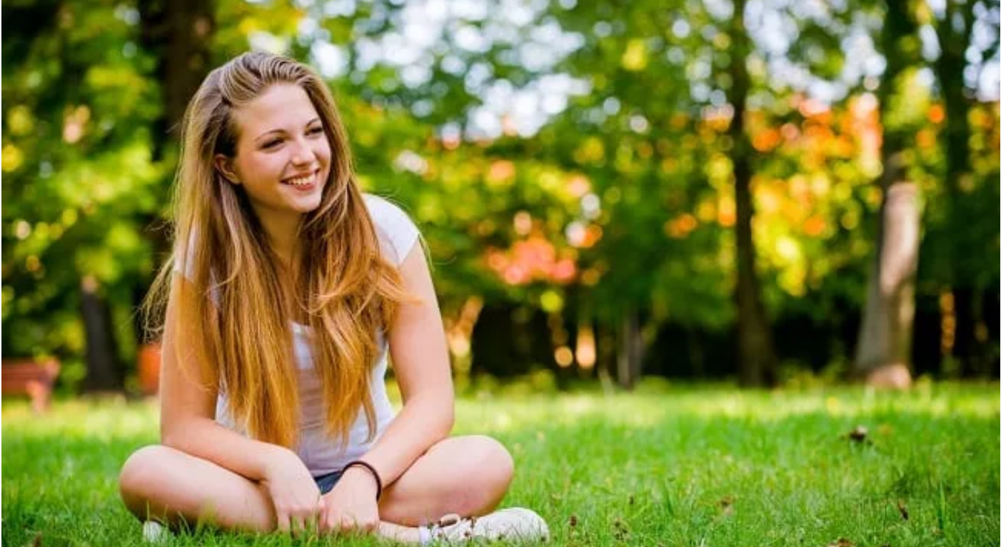 Young woman sitting in the grass at a park smiling