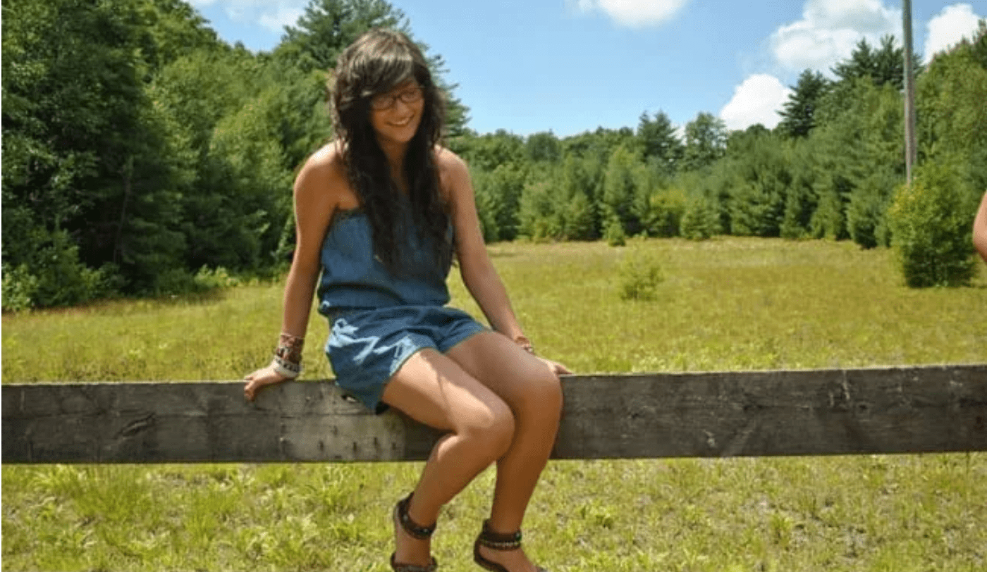 Young woman sitting on a wooden fence beam