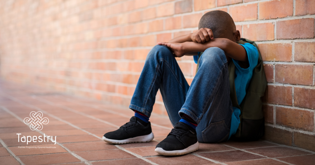 Young child sitting on the ground in distress with his head laid on his folded arms