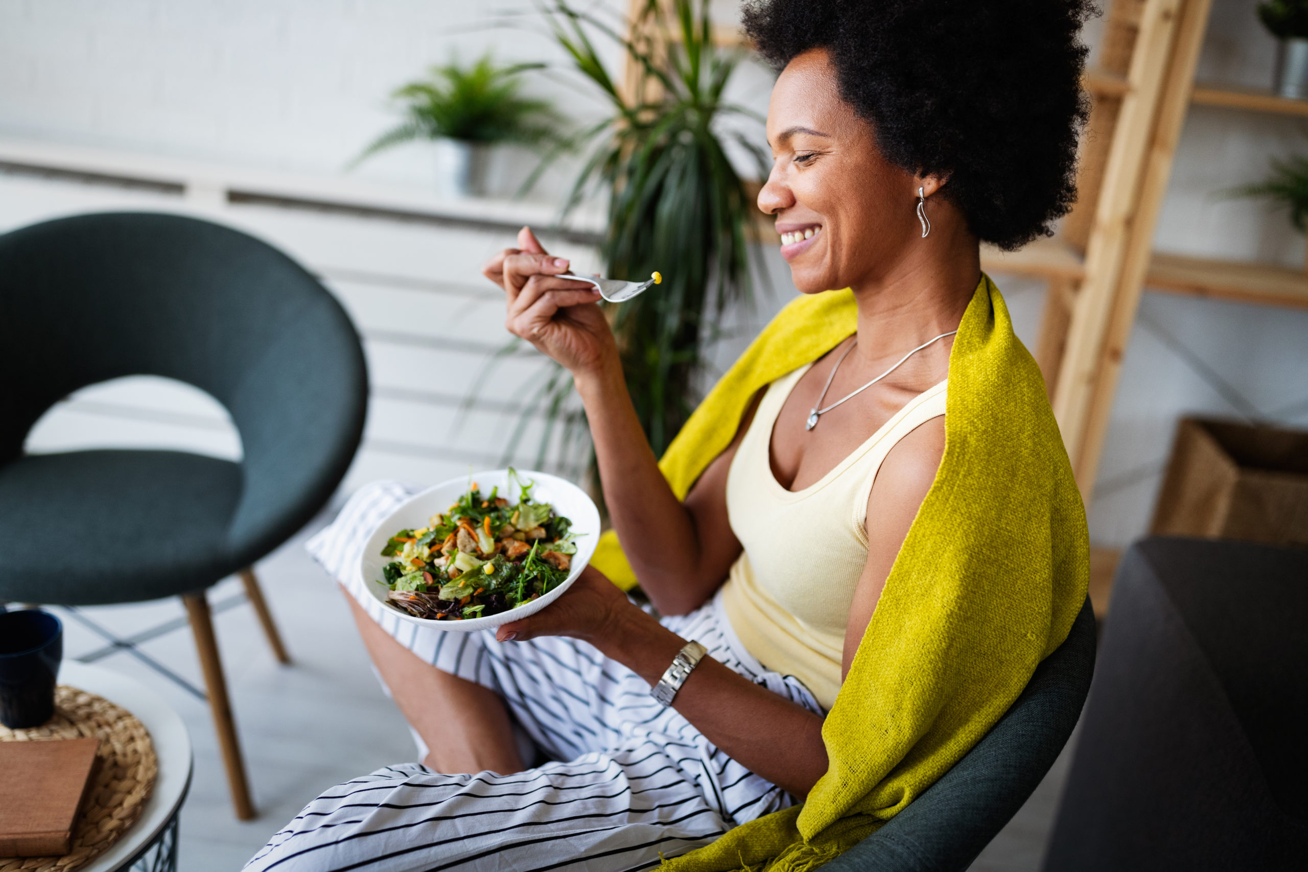 Cheerful afro american woman eating fresh vegetable salad at home.
