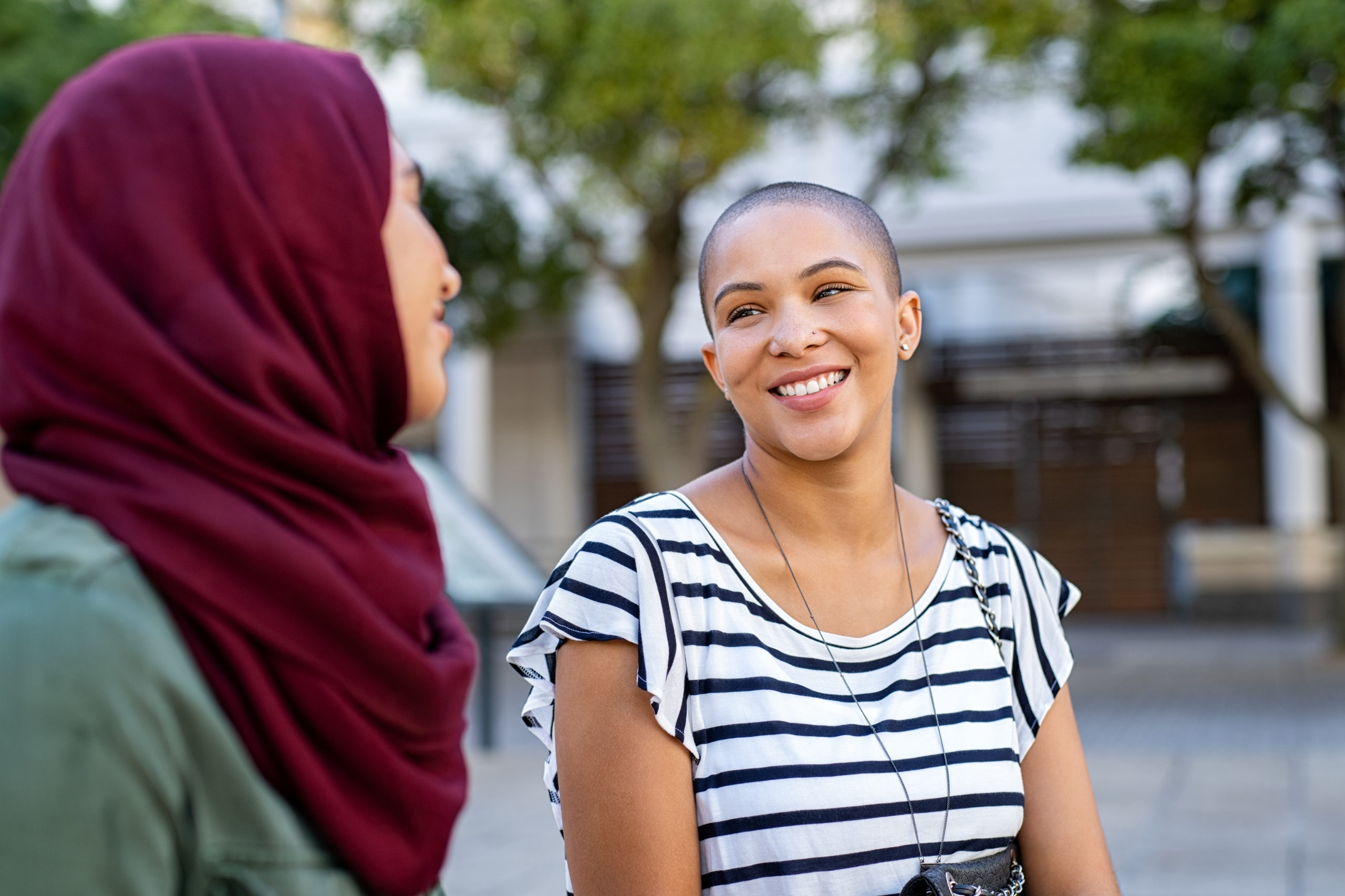 Cheerful african american woman in conversation with muslim girl. Happy multiethnic friends in street looking at each other while in a conversation. Beautiful woman with friend in hijab talking to each others.