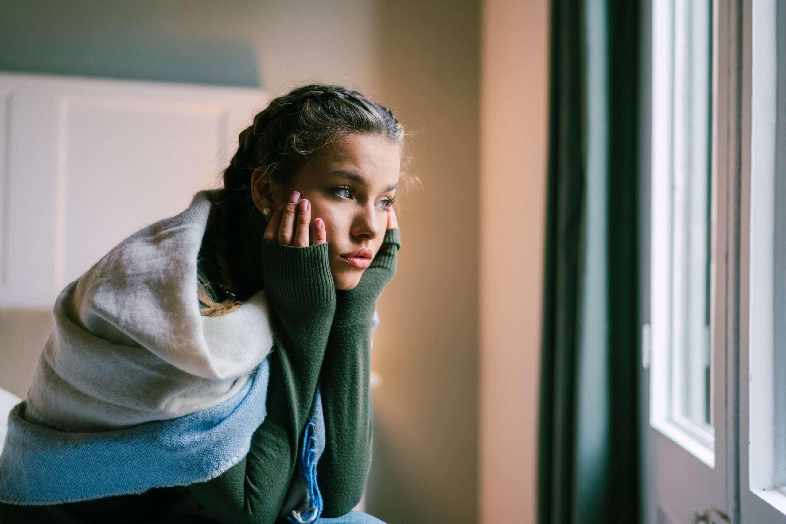 Young woman sitting on the bed looking out the window