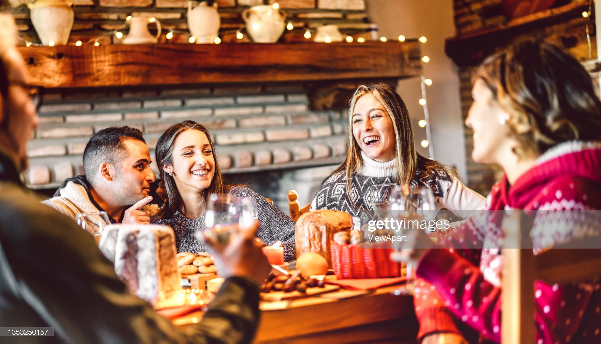 Millenial people tasting Christmas sweets at home supper party - New year's eve and winter holiday concept with young friends having fun eating together at evening - Bulb string lights warm filter