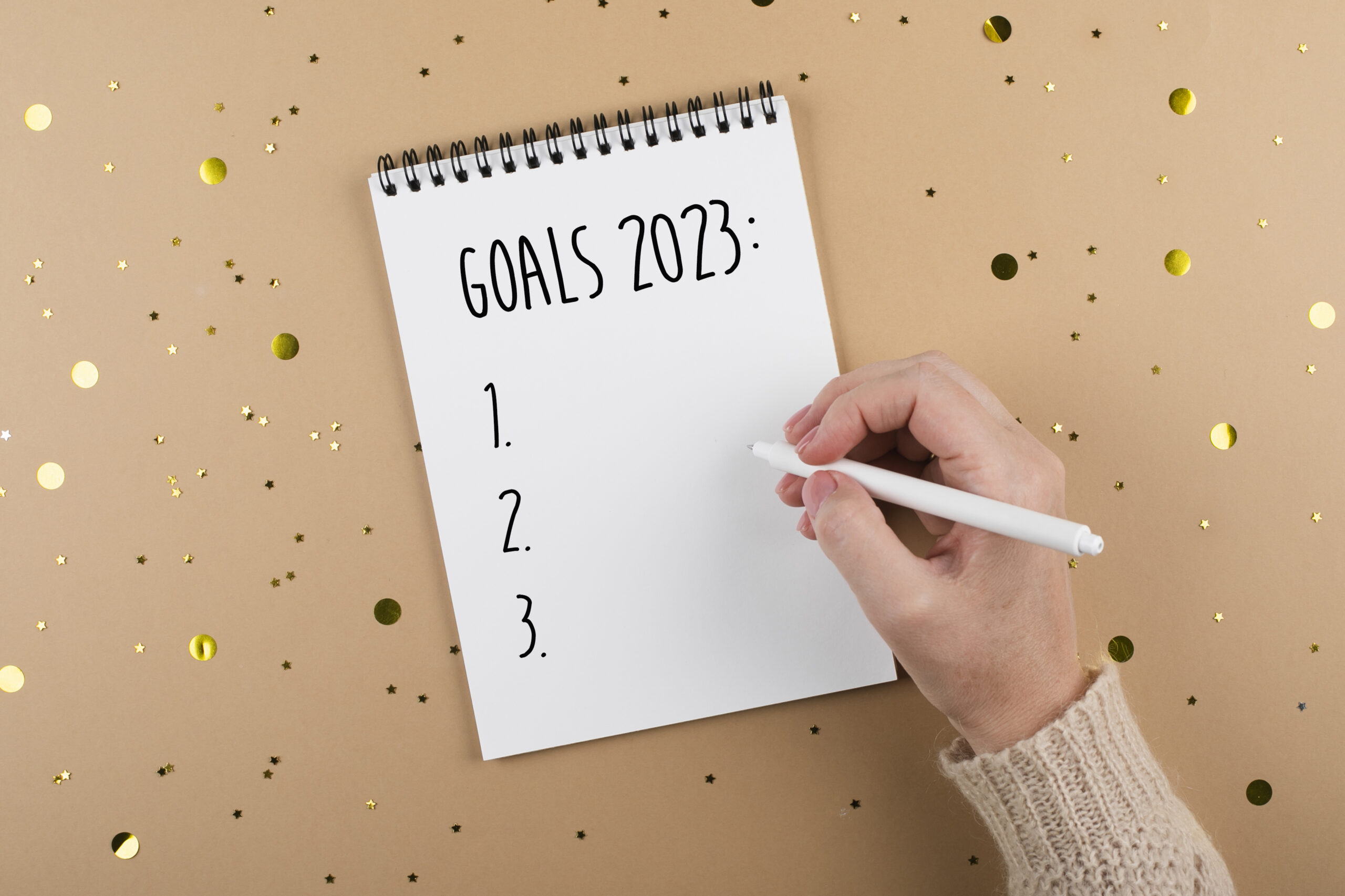 New Year goals 2023. Woman's hand writing in note pad goals list. Concept of new year planning. Flat lay, top view