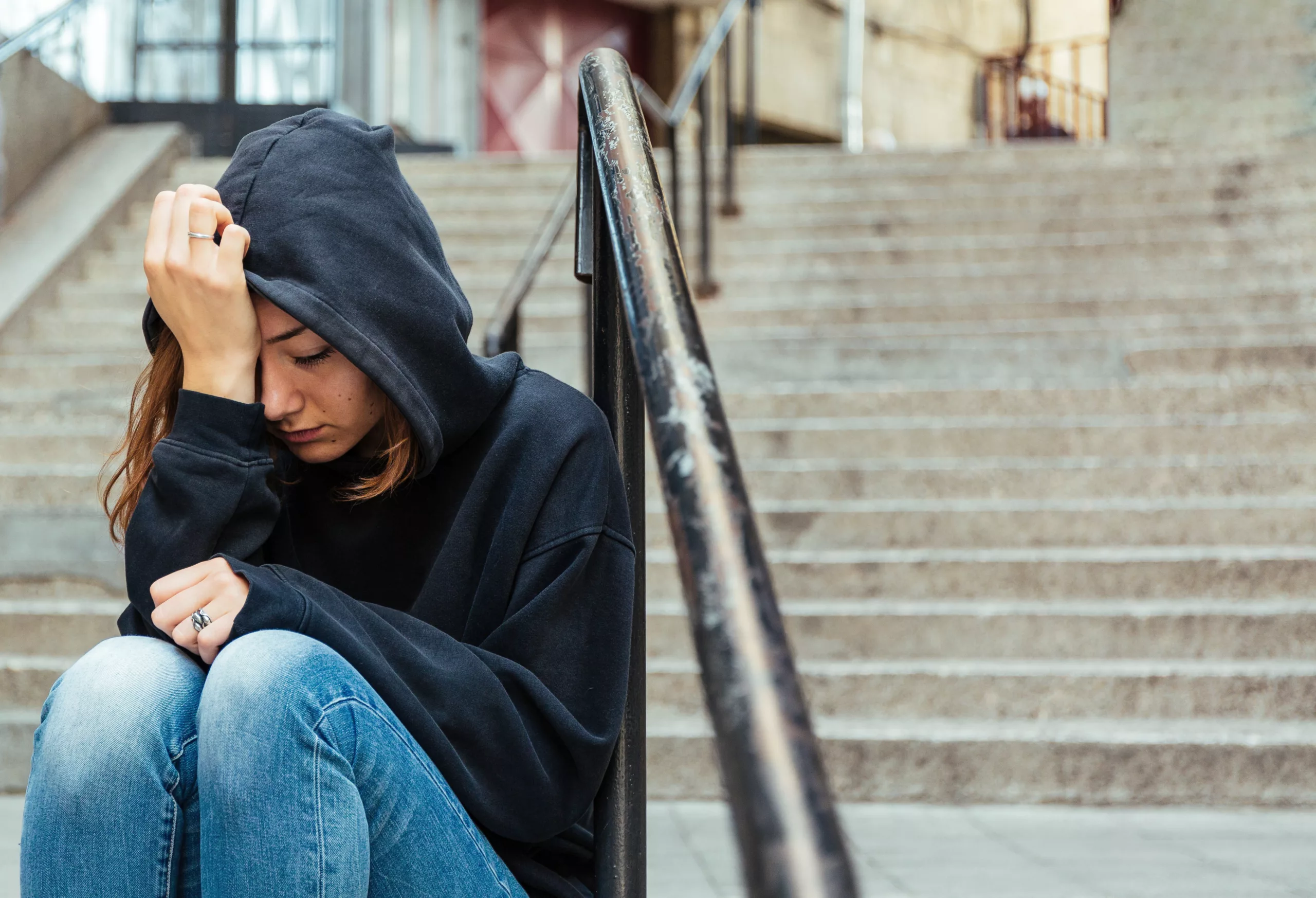 Teenage girl sitting outdoors on the staircase covering her head with sweatshirt hood