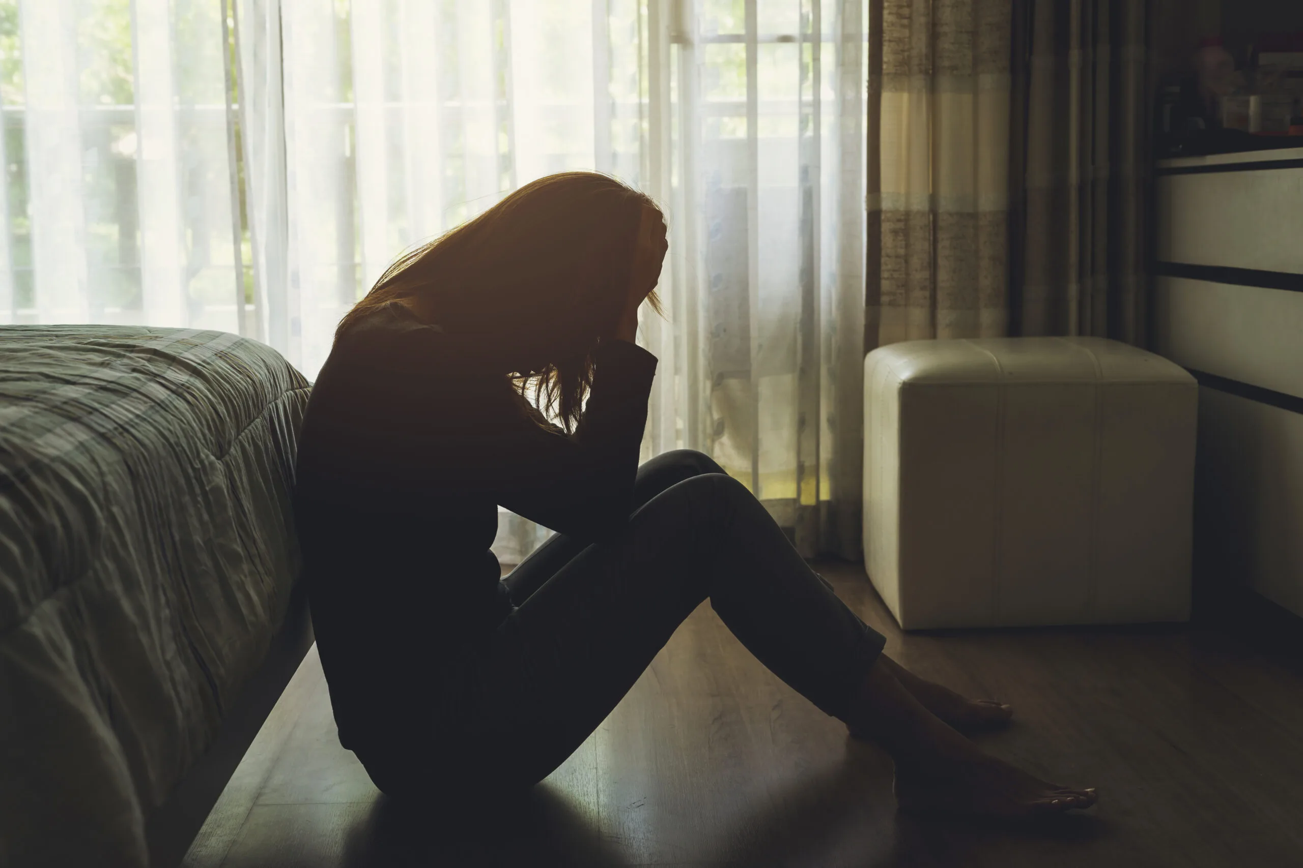 depressed woman sitting head in hands in the dark bedroom