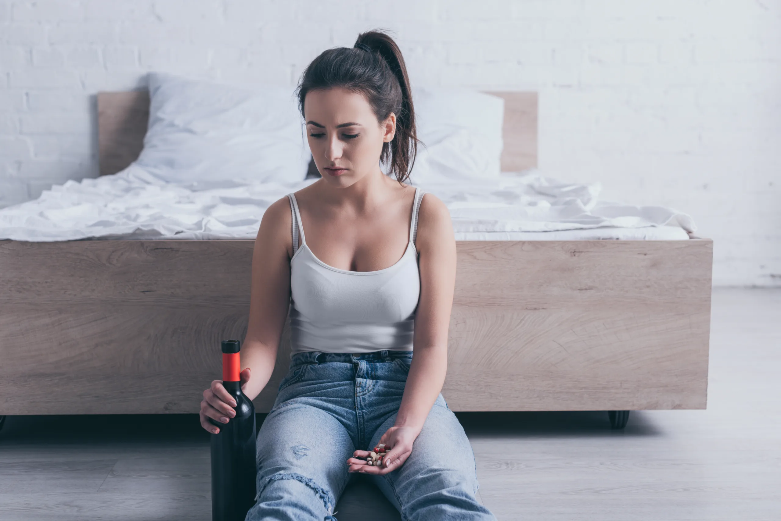 frustrated young woman sitting on floor with bottle of alcohol