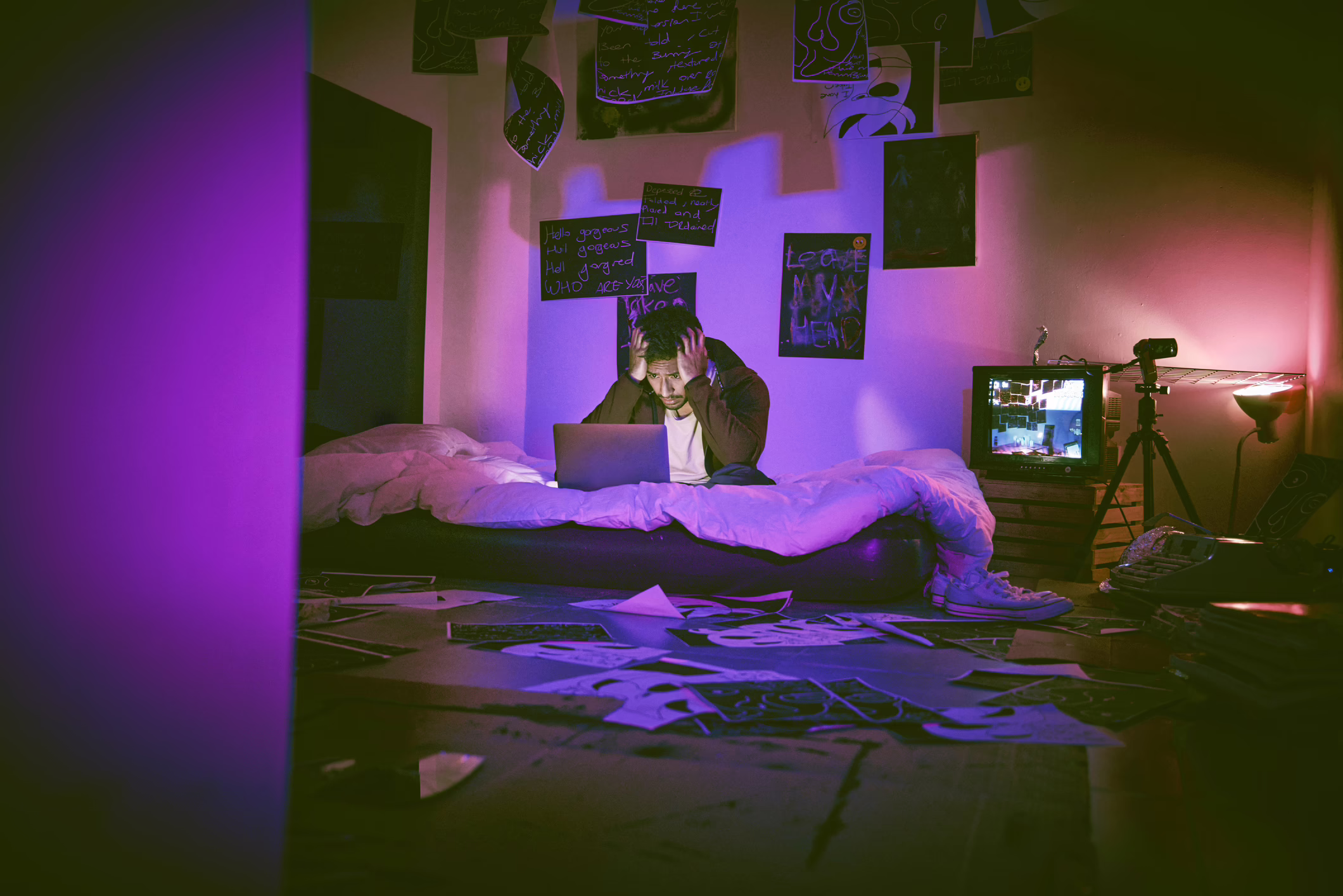 man hallucinating and feeling paranoid while using his laptop in his messy bedroom at home. Young man feeling stressed and scared. Schizophrenic thinking he's getting hacked through technology